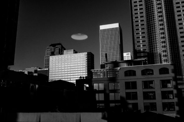 a skyline in greyscale with a ufo floating overhead